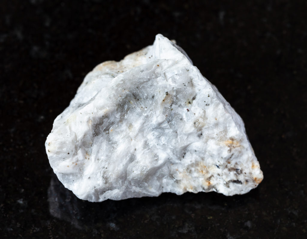 A chunk of unpolished Barite (Baryte) ore that is white, flecked with iron and veined with other igneous components.